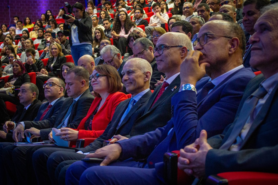 big tech self-regulation — Audience members seated in a conference hall watching a presentation.